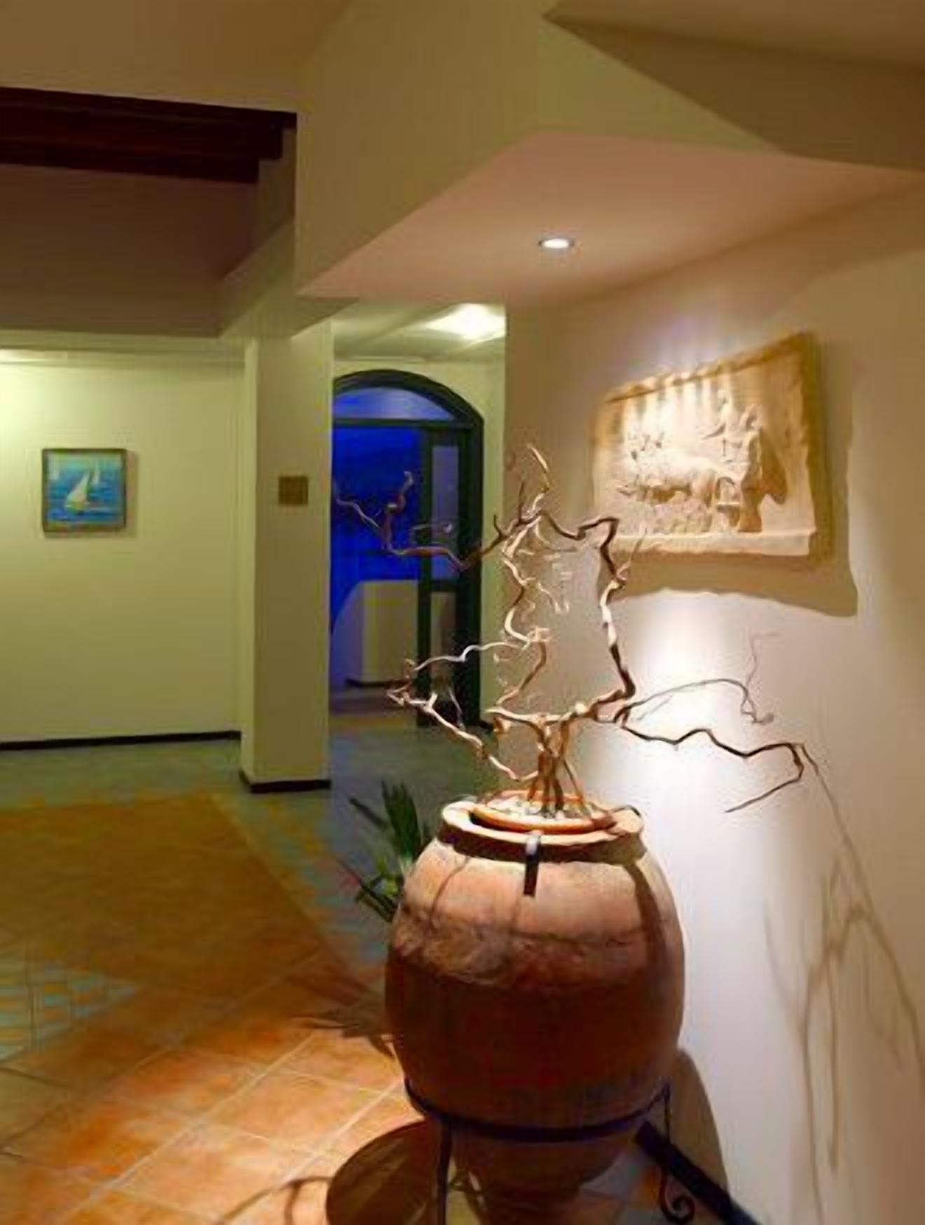 Un pasillo con una escultura de gran jarra, una obra de arte enmarcada y suelo de baldosas.