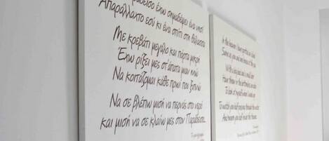 Un dormitori amb un capçal de fusta, roba de llit blanca i un coixí groc. Hi ha dues frases emmarcades a la paret.