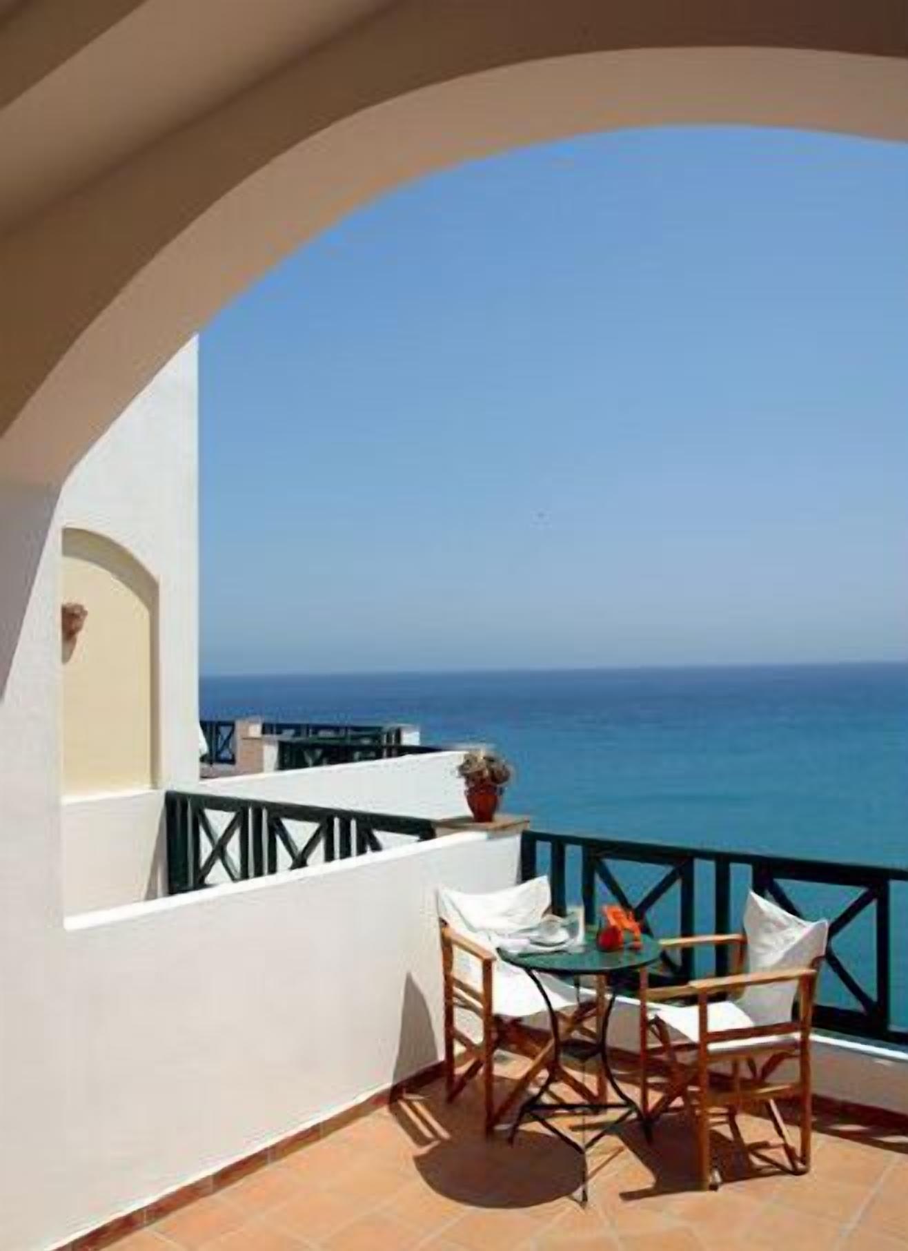 A balcony with a table and chairs, overlooking a clear blue sea.