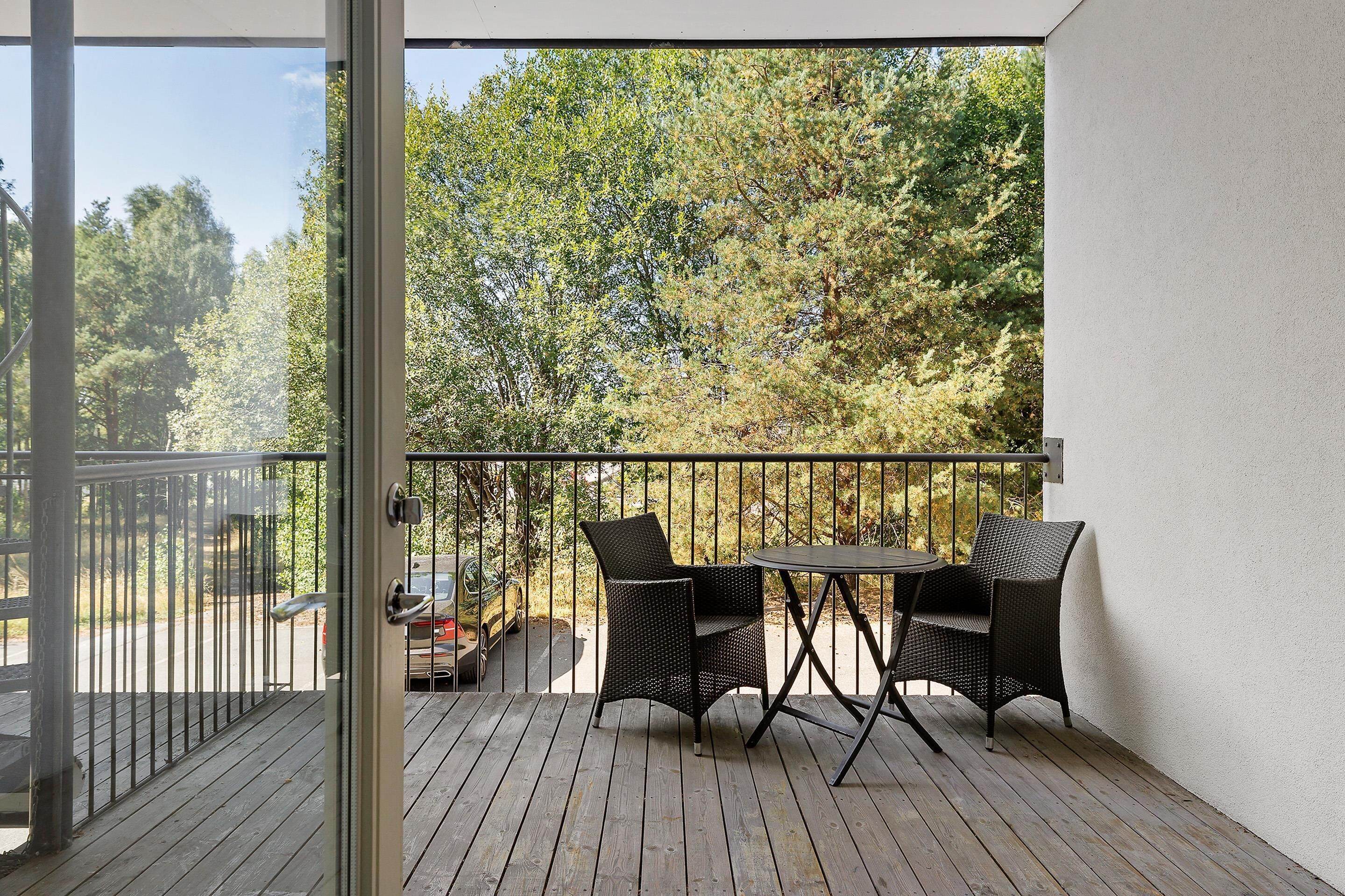 A balcony with a wooden floor, metal railing, and two wicker chairs with a small round table.