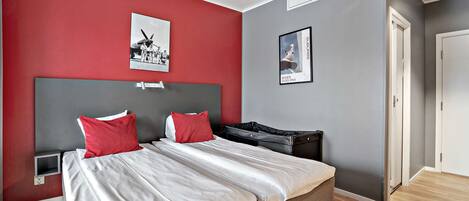 A modern hotel room with a large bed, two red pillows, a grey headboard, and a small bedside table.