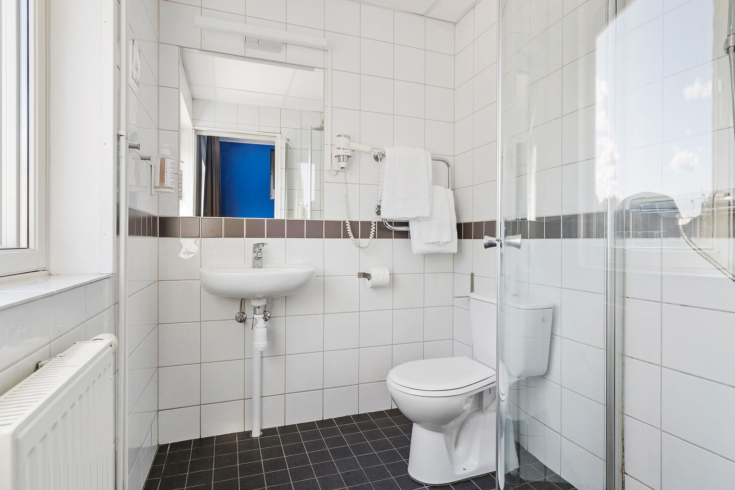 A small, modern bathroom with a white sink, toilet, and shower.