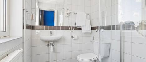 Uma casa de banho pequena e moderna, com lavatório, sanita e chuveiro, todos brancos.