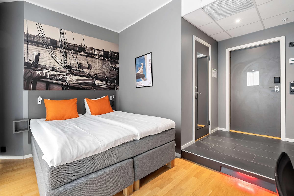 Une chambre d’hôtel moderne comprenant un lit, une œuvre d’art accrochée au mur, une porte et une petite table de chevet.