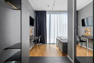 Una habitación de hotel moderna con cama, escritorio, silla, televisor y un amplio ventanal con cortinas.