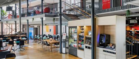 Un espace intérieur à plusieurs niveaux, comprenant des coins salon, un distributeur automatique et un escalier.
