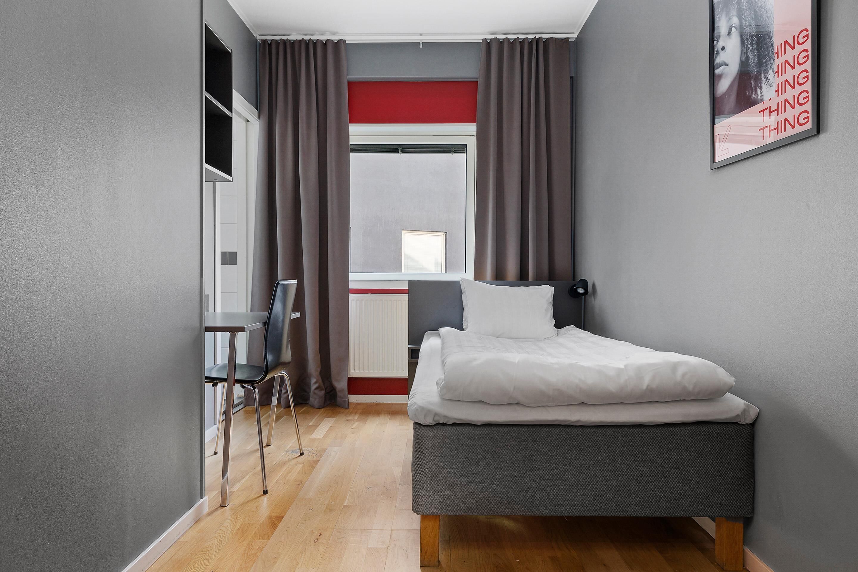 Une chambre à coucher avec un lit, une chaise, un bureau et une fenêtre avec des rideaux.