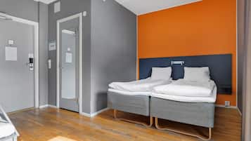 A hotel room with a double bed, a wooden floor, a grey and orange wall, and a white door.