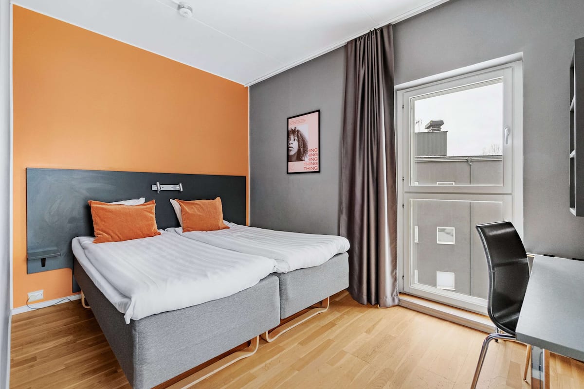 Une chambre d’hôtel moderne, équipée d’un lit, d’un bureau et d’une fenêtre.