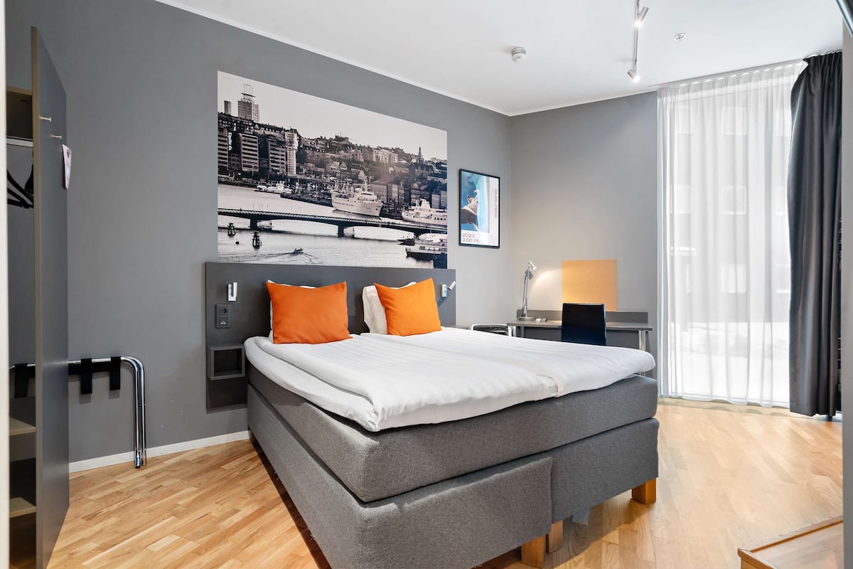 Une chambre d’hôtel moderne avec un grand lit, un bureau et un tableau représentant un paysage urbain accroché au mur.