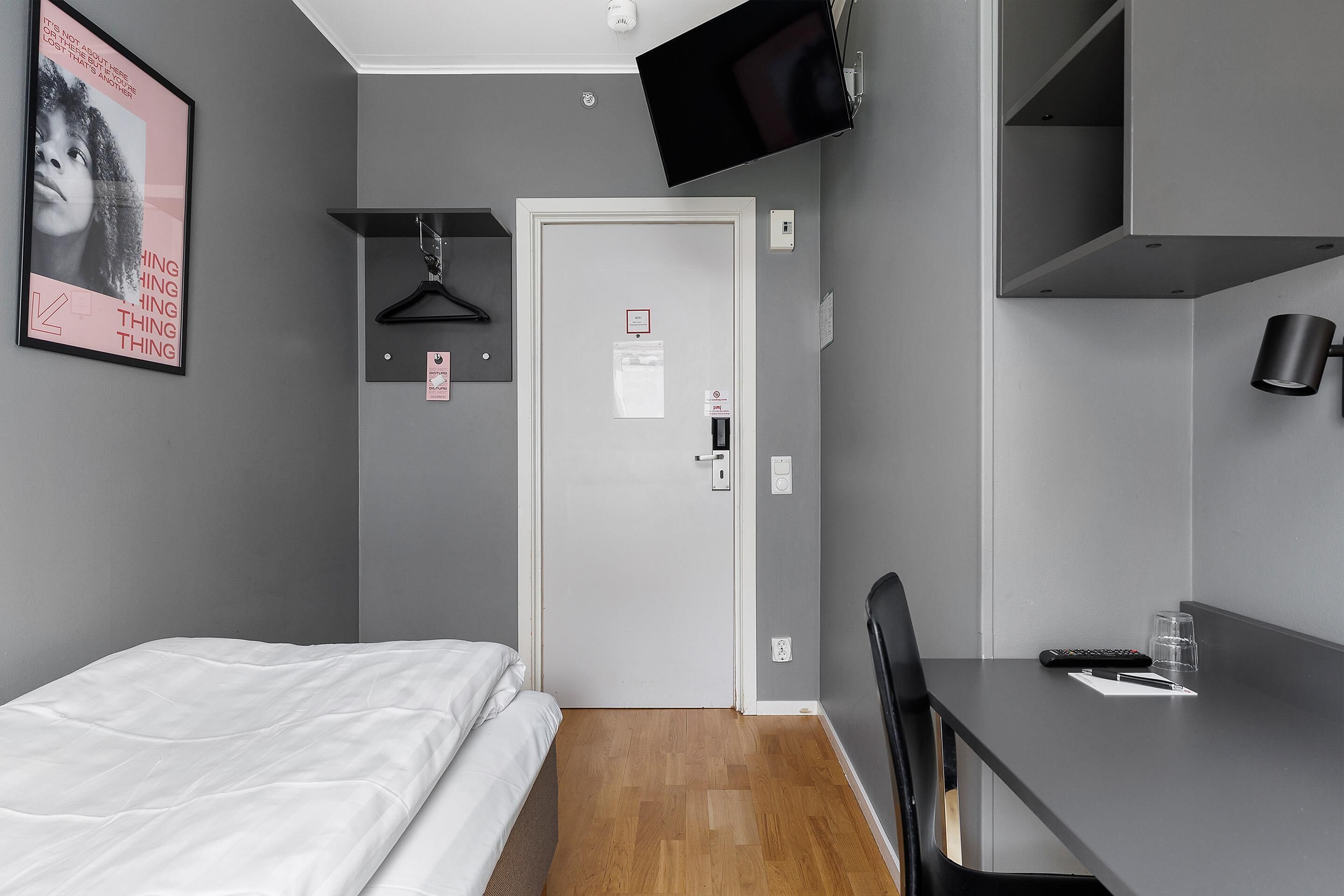 Een hotelkamer met een bed, een bureau, een stoel, een televisie en een deur met een bordje.