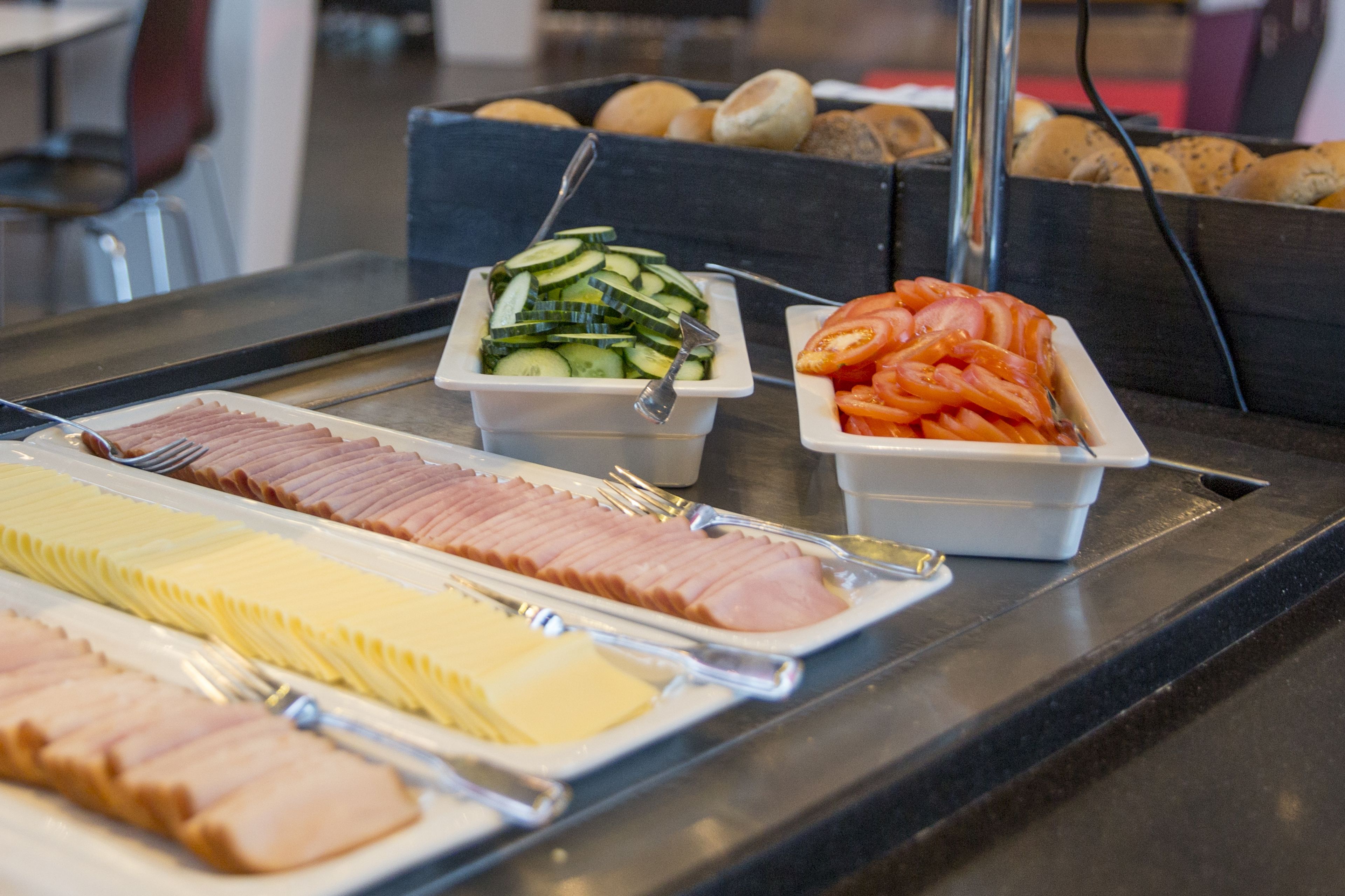 A buffet table with various food items including sliced ham, cheese, cucumbers, and tomatoes.