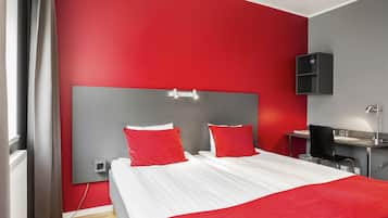 Ein modernes Schlafzimmer mit rotem und grauem Farbschema, ausgestattet mit einem großen Bett mit roten Kissen, einem Nachttisch und einem Schreibtisch mit einer Lampe.