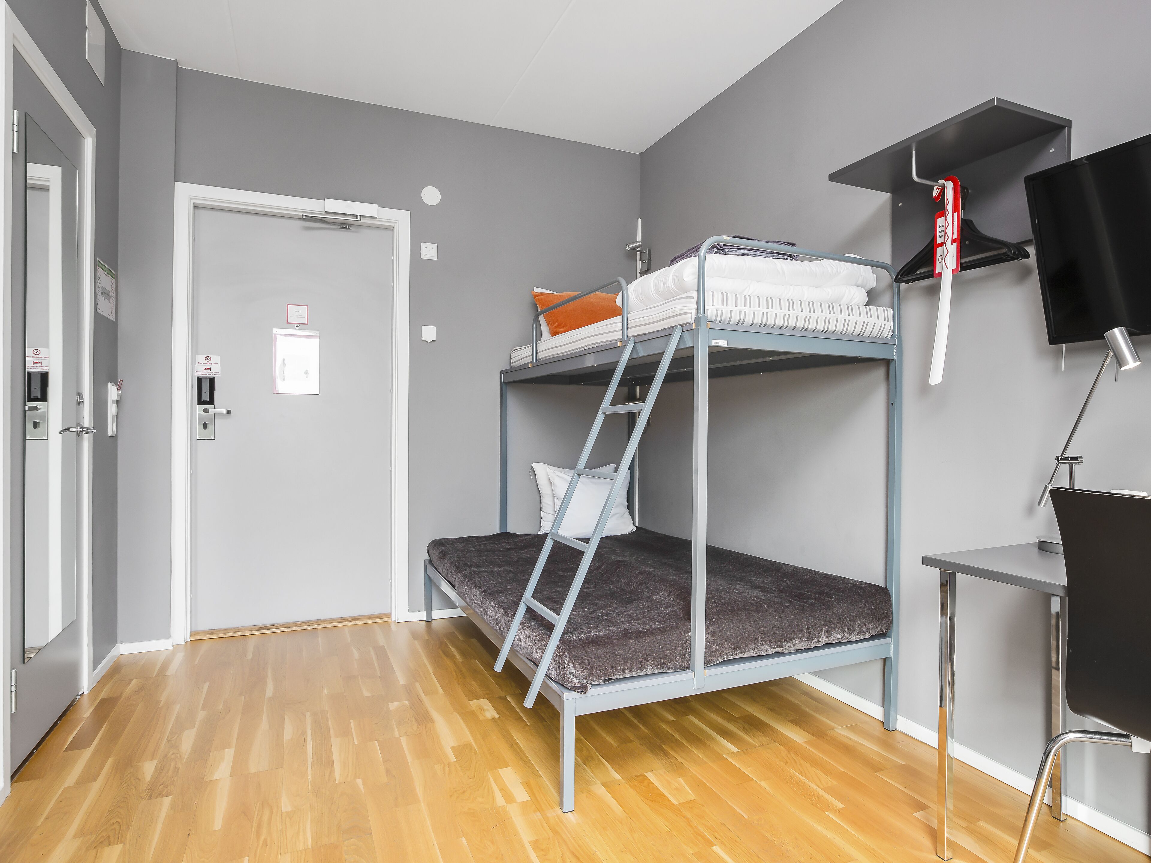 A bunk bed with a desk and chair, a television, and a door with a sign.