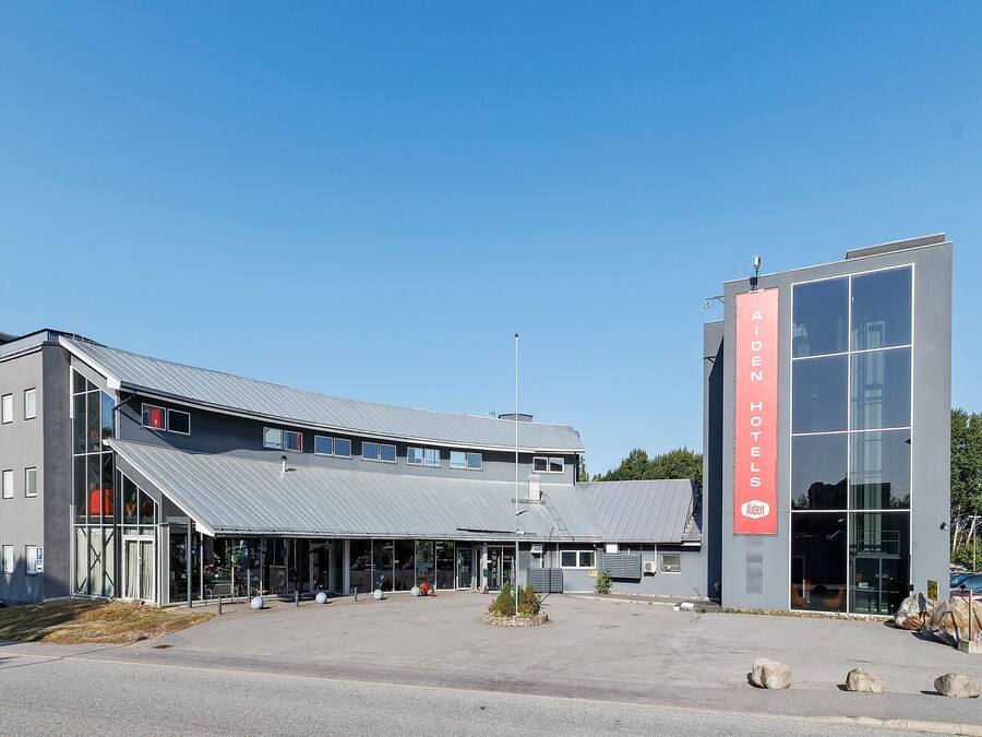 Um edifício moderno de hotel com um sinalização chamativa Aiden Hotels, uma entrada coberta e área de estacionamento.