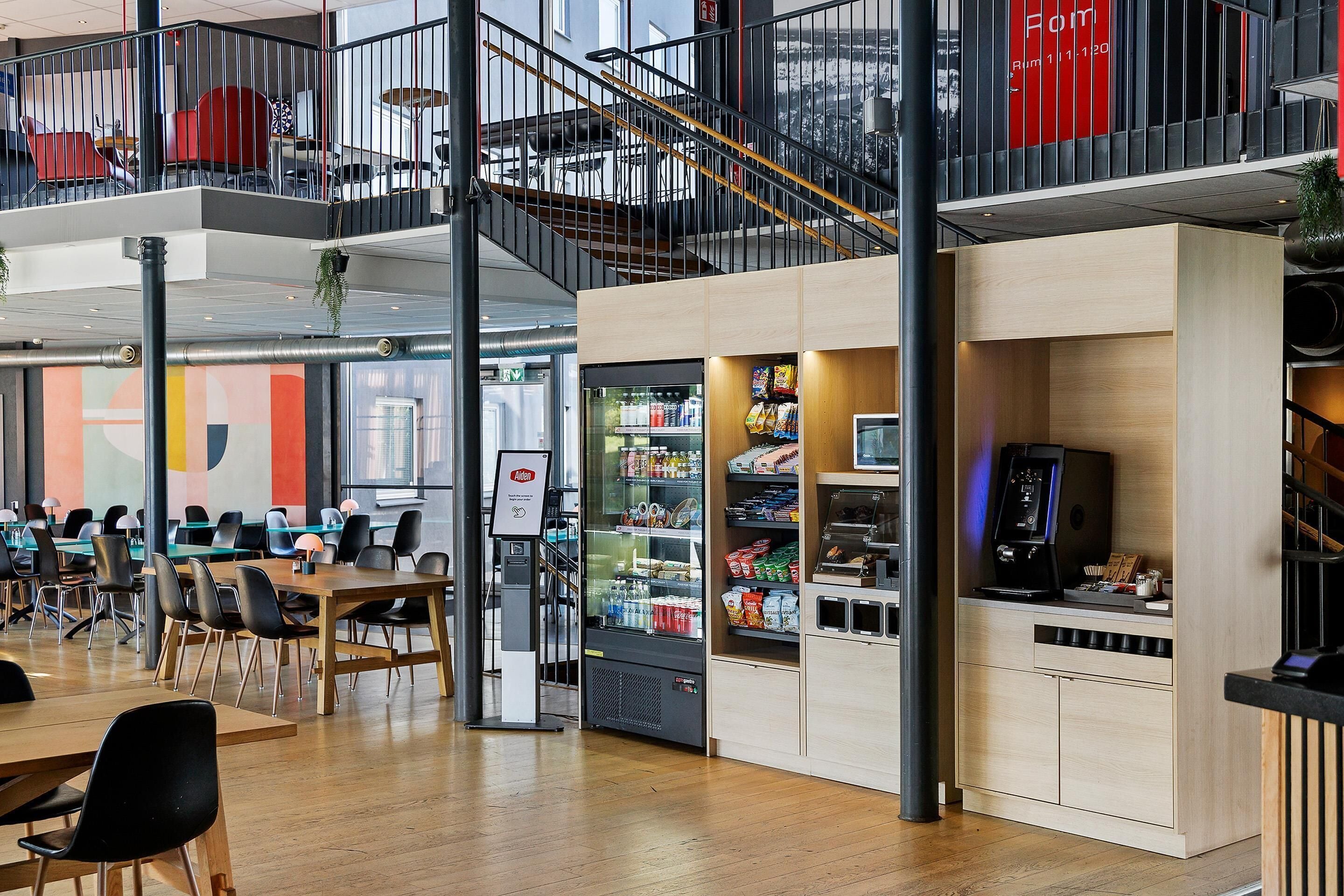 A modern indoor space with a dining area, vending machines, and a staircase.