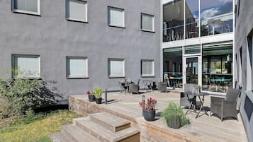Un edificio con varias ventanas, mesas al aire libre y una terraza de madera.