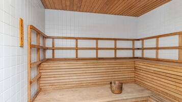 A wooden sauna with a sloped seating area and a small bucket.