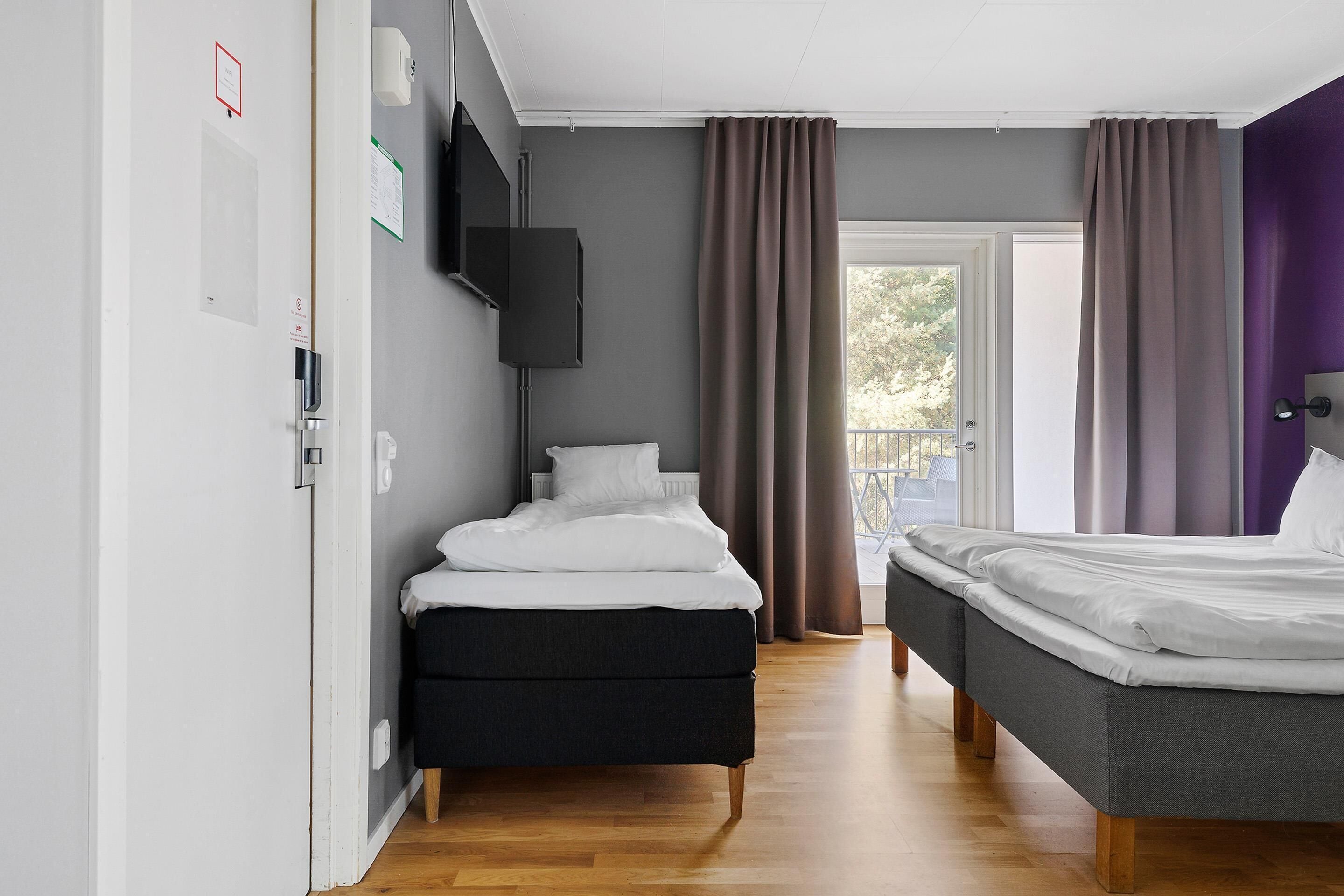 Un dormitorio moderno con dos camas, una televisión de pantalla plana y un balcón con cortinas.