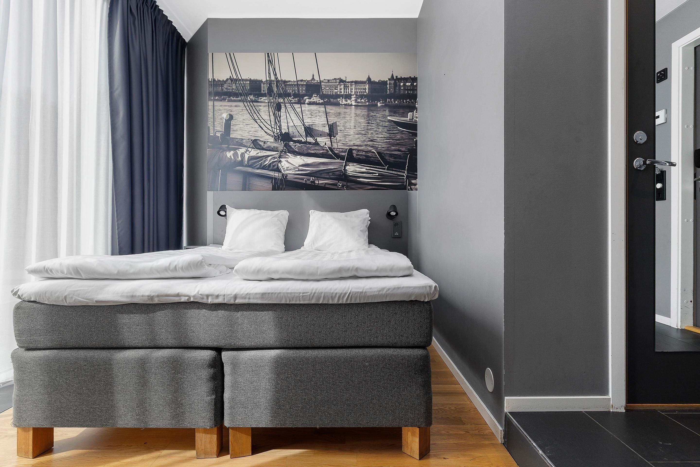 Quarto moderno com uma cama, uma pintura de paisagem urbana e uma porta à direita.