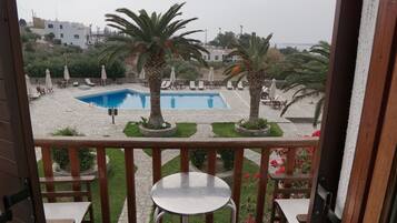 Un espace piscine avec des chaises longues et des palmiers, vu depuis un balcon équipé d’une table et de chaises.