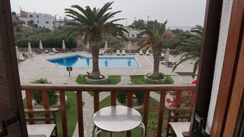 Un espace piscine avec des chaises longues et des palmiers, vu depuis un balcon équipé d’une table et de chaises.