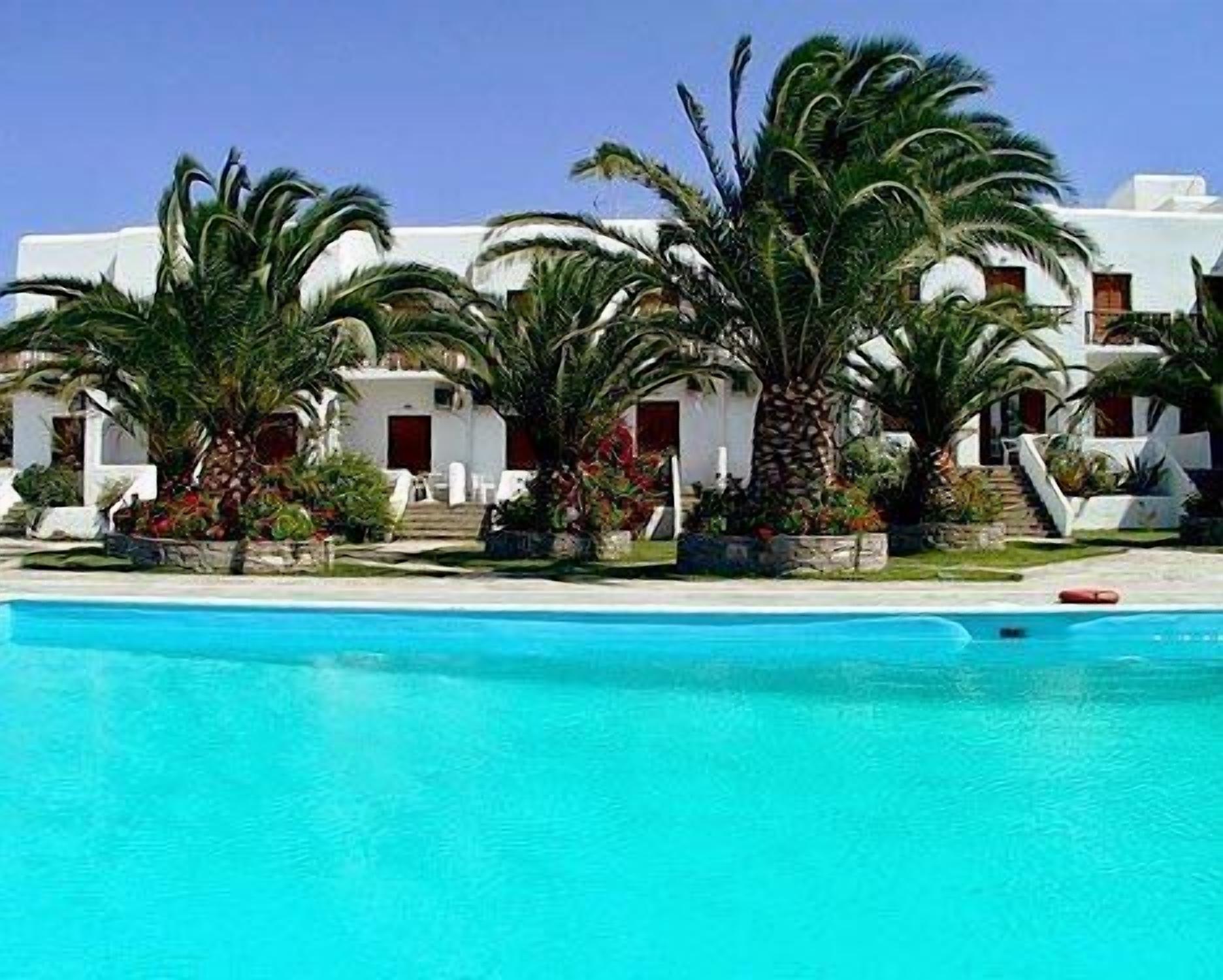 A poolside view of a resort with white buildings, palm trees, and a clear blue pool.