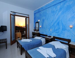 A hotel room with two beds, a TV, a balcony with a view of the sunset, and a blue textured wall.