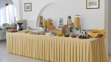 A buffet table with various food items and beverages, set in a room with white walls and framed pictures.