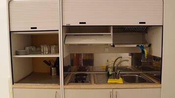 A compact kitchen with a sink, stove, and shelves.