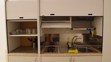 A compact kitchen with a sink, stove, and shelves.