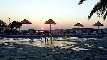 A pool area with lounge chairs and umbrellas, surrounded by stone tiles and palm trees.