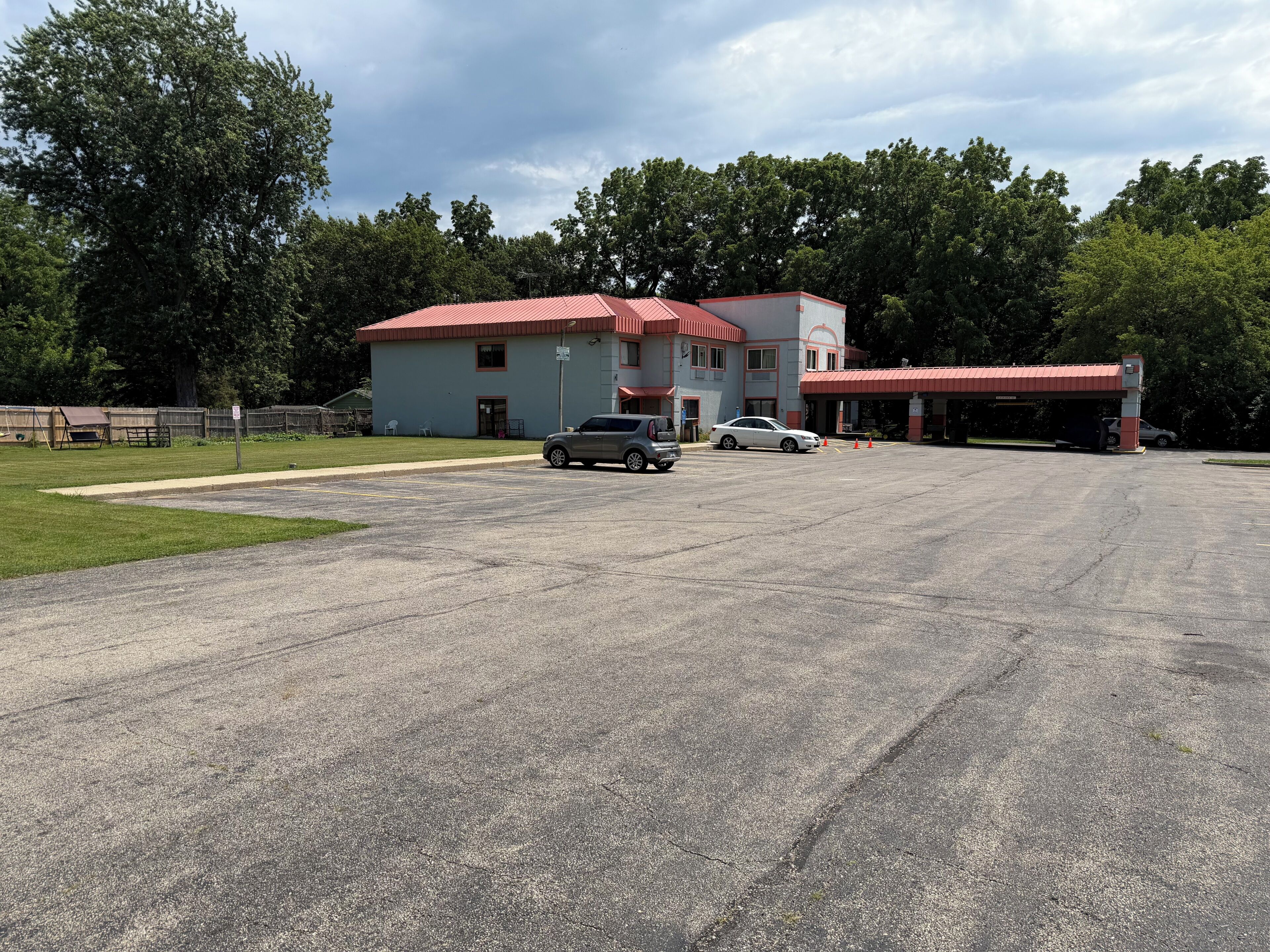 Un bâtiment avec un toit rouge, un parking et une zone herbeuse.