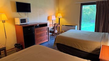 A hotel room with a bed, a desk with a computer, a TV, a lamp, and a window with curtains.