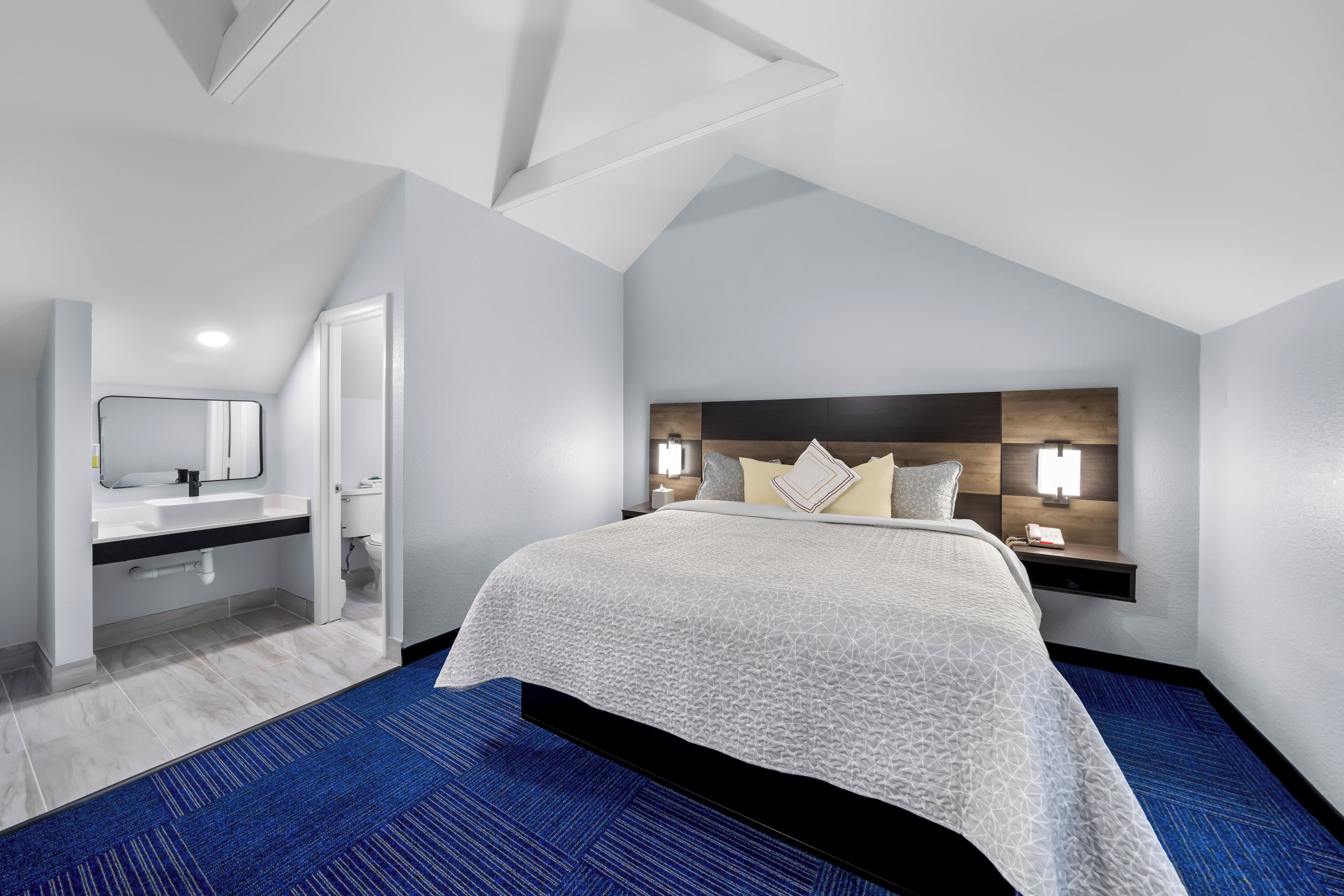 Una habitación de hotel moderna con una cama grande, un escritorio integrado, un tocador con espejo y un baño.