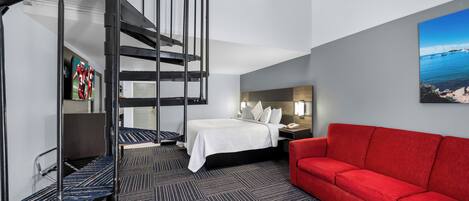 A hotel room with a spiral staircase, a bed, a red sofa, and a painting of a coastal scene.