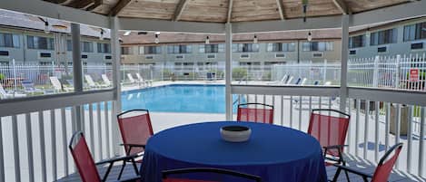 Un espacio exterior techado con una piscina, sillas rojas y una mesa con un bol.