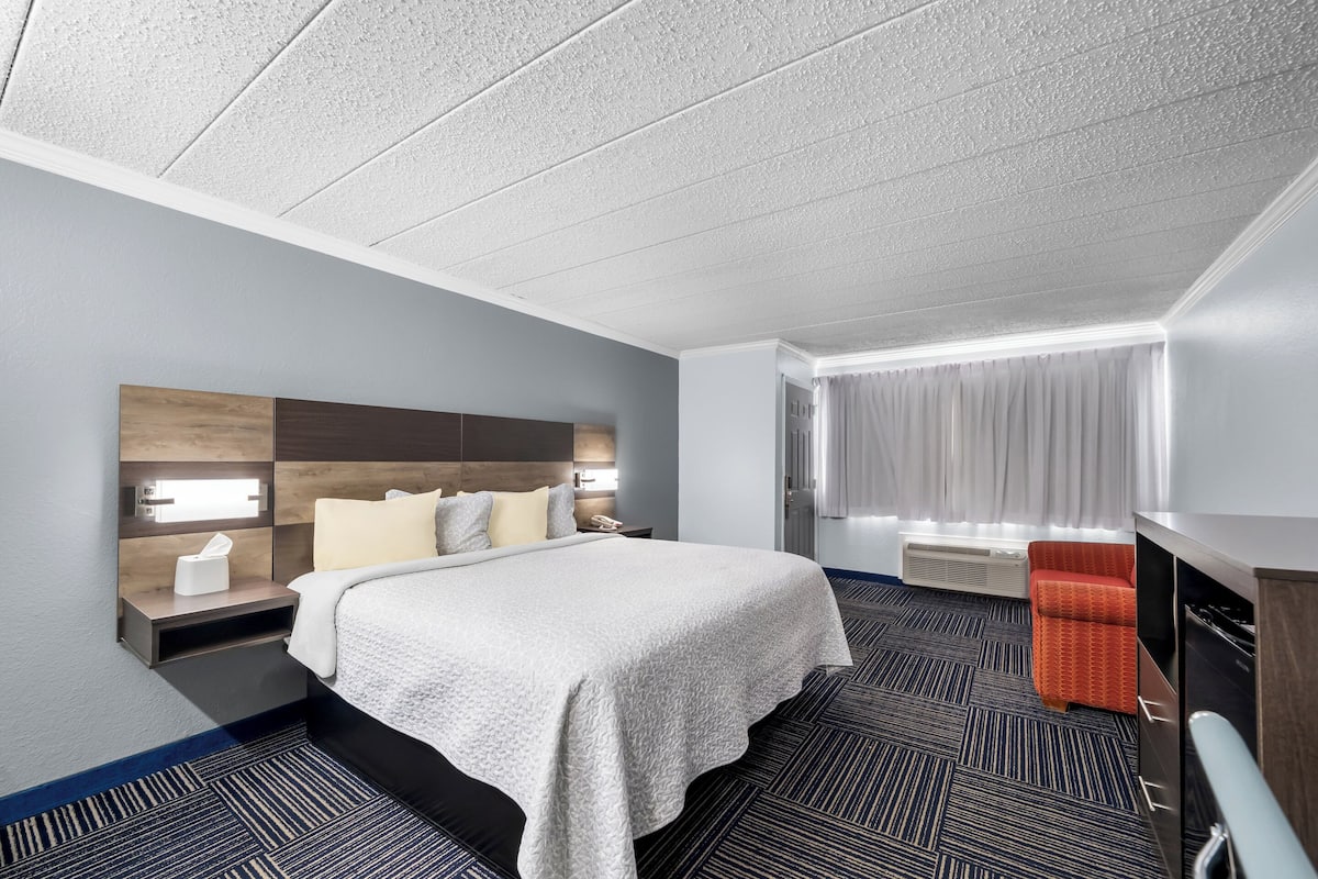 A hotel room with a large bed, a nightstand with a lamp, a TV, and a window with curtains.