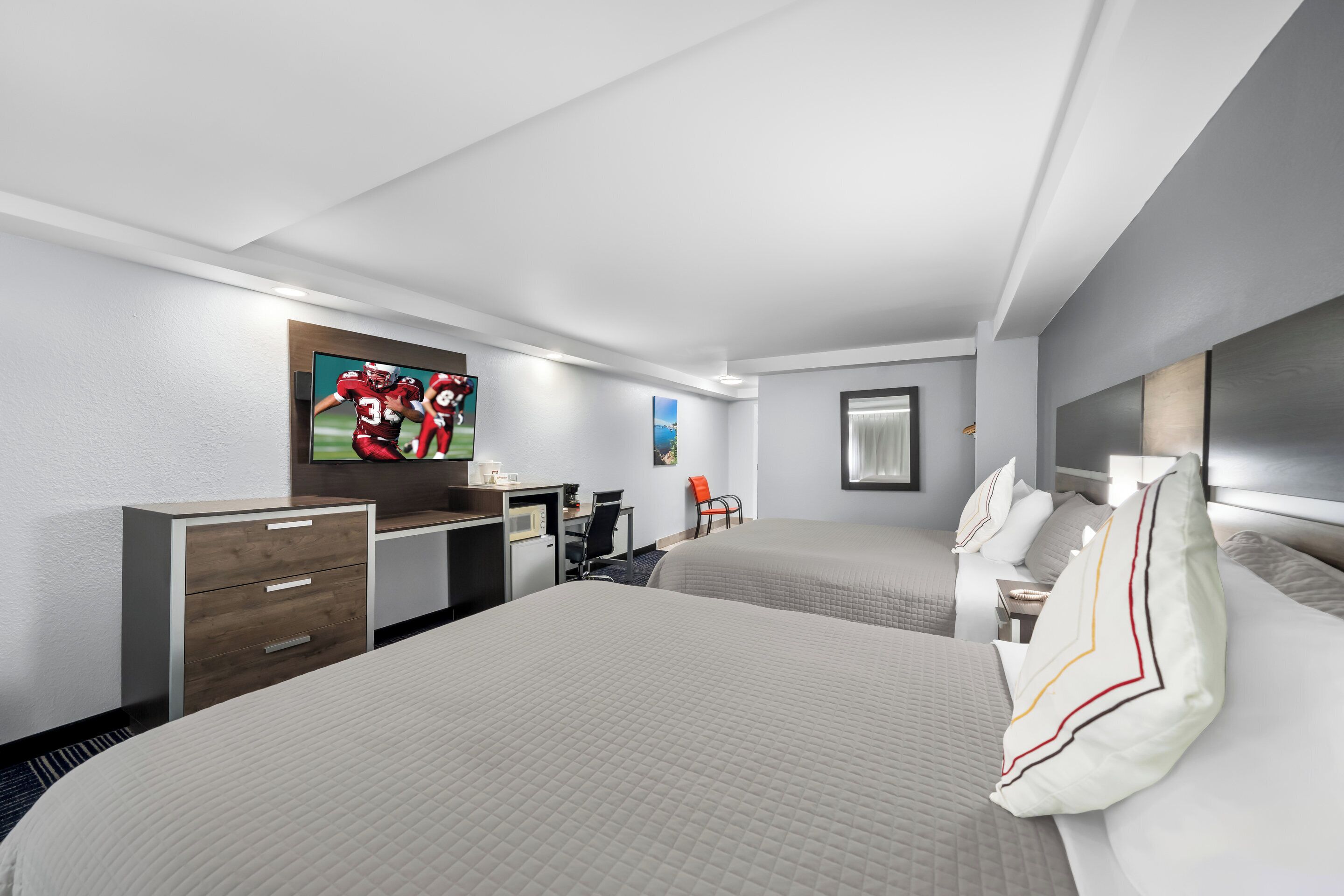 Habitación de hotel con dos camas, un escritorio, una silla y un televisor mostrando un partido deportivo.