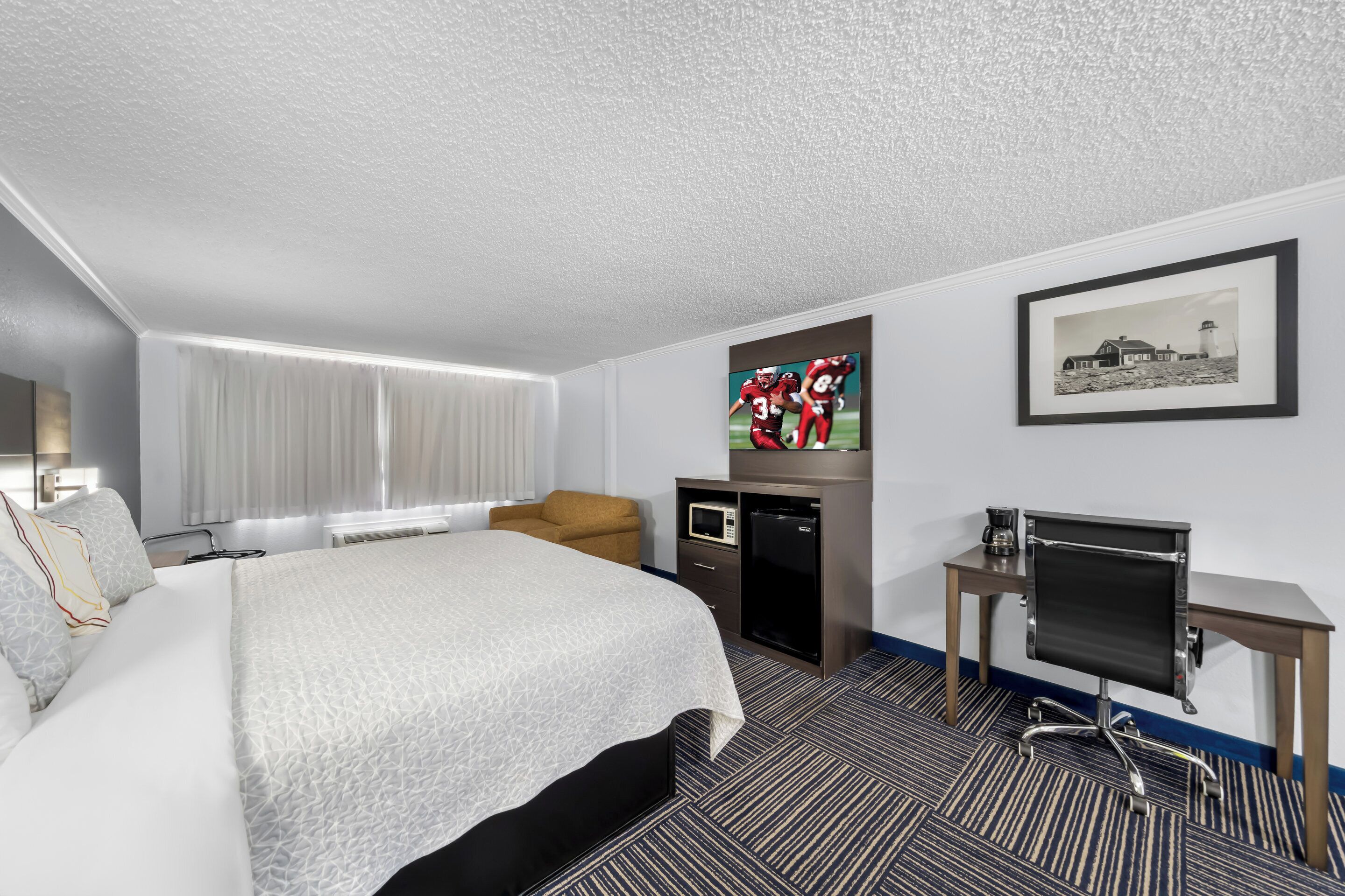 Une chambre d’hôtel avec un grand lit, un bureau avec un ordinateur, une télévision et un tableau encadré au mur.