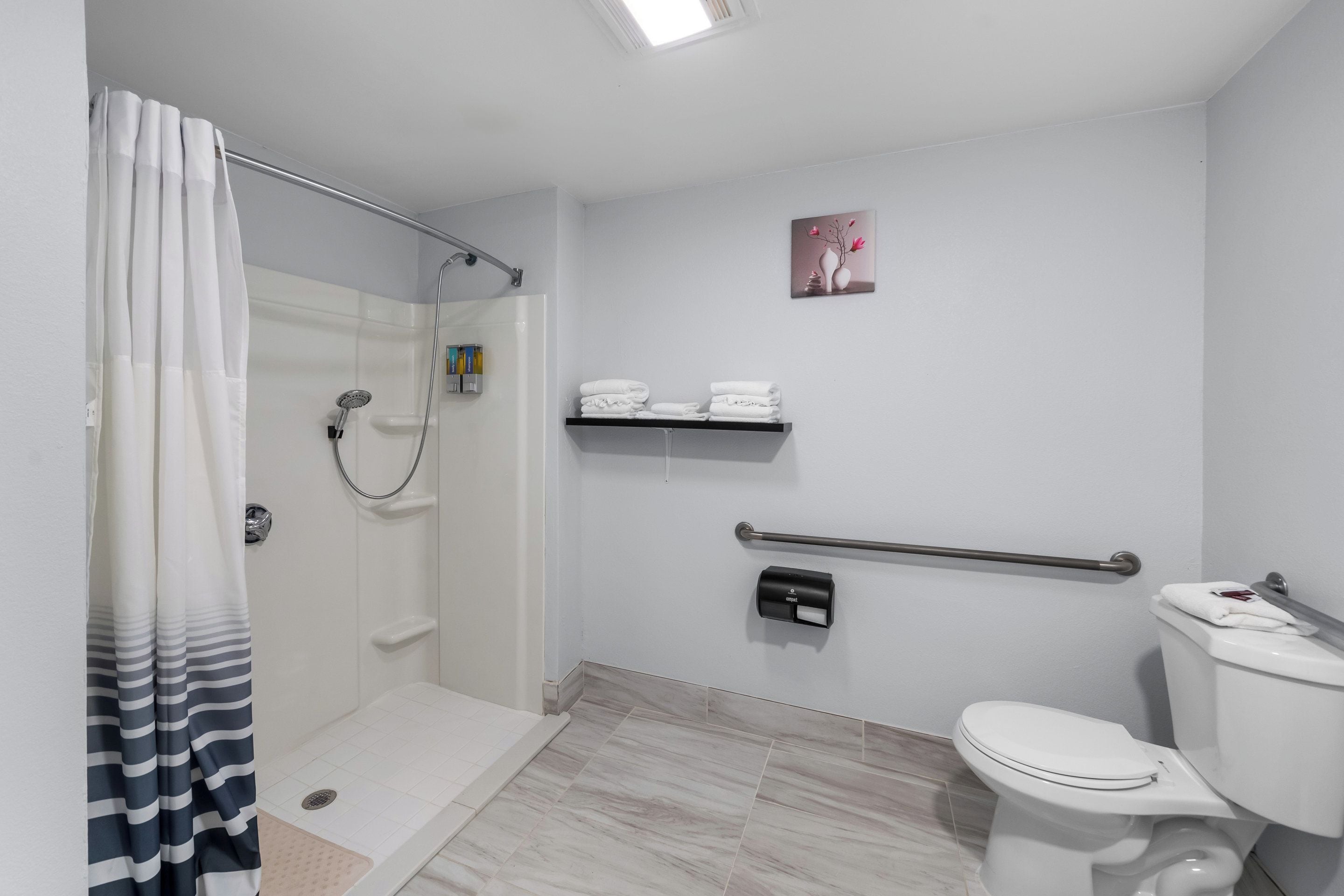 A modern bathroom with a shower, toilet, and handrails.