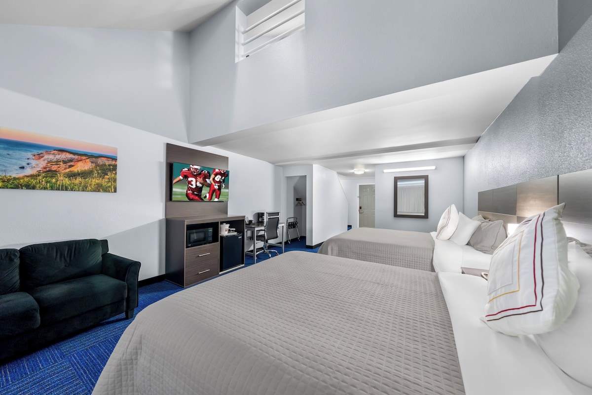 A hotel room with a large bed, a sofa, a desk, a TV, and a painting on the wall.