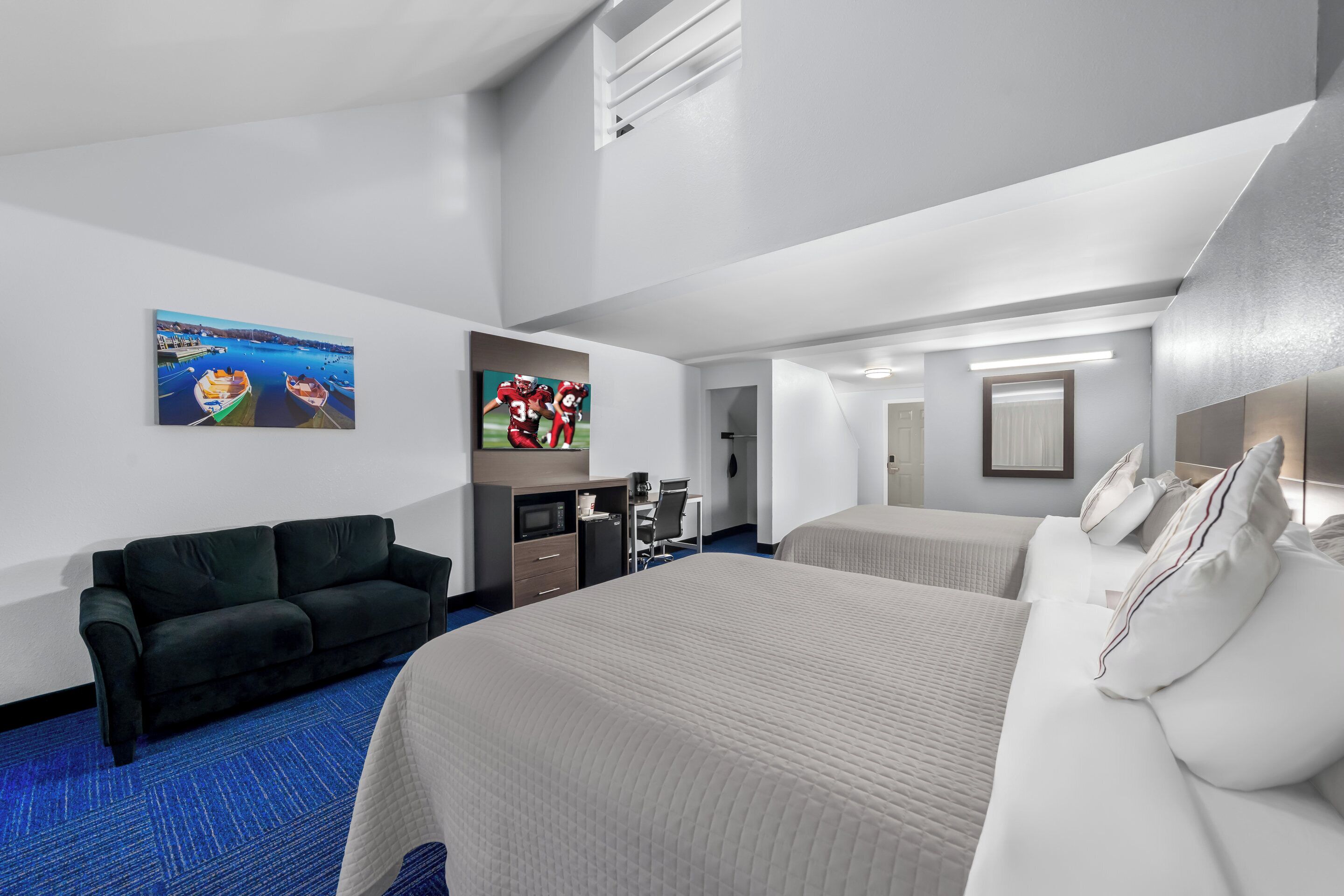 A hotel room with a large bed, a sofa, a desk with a computer, and artwork on the walls.