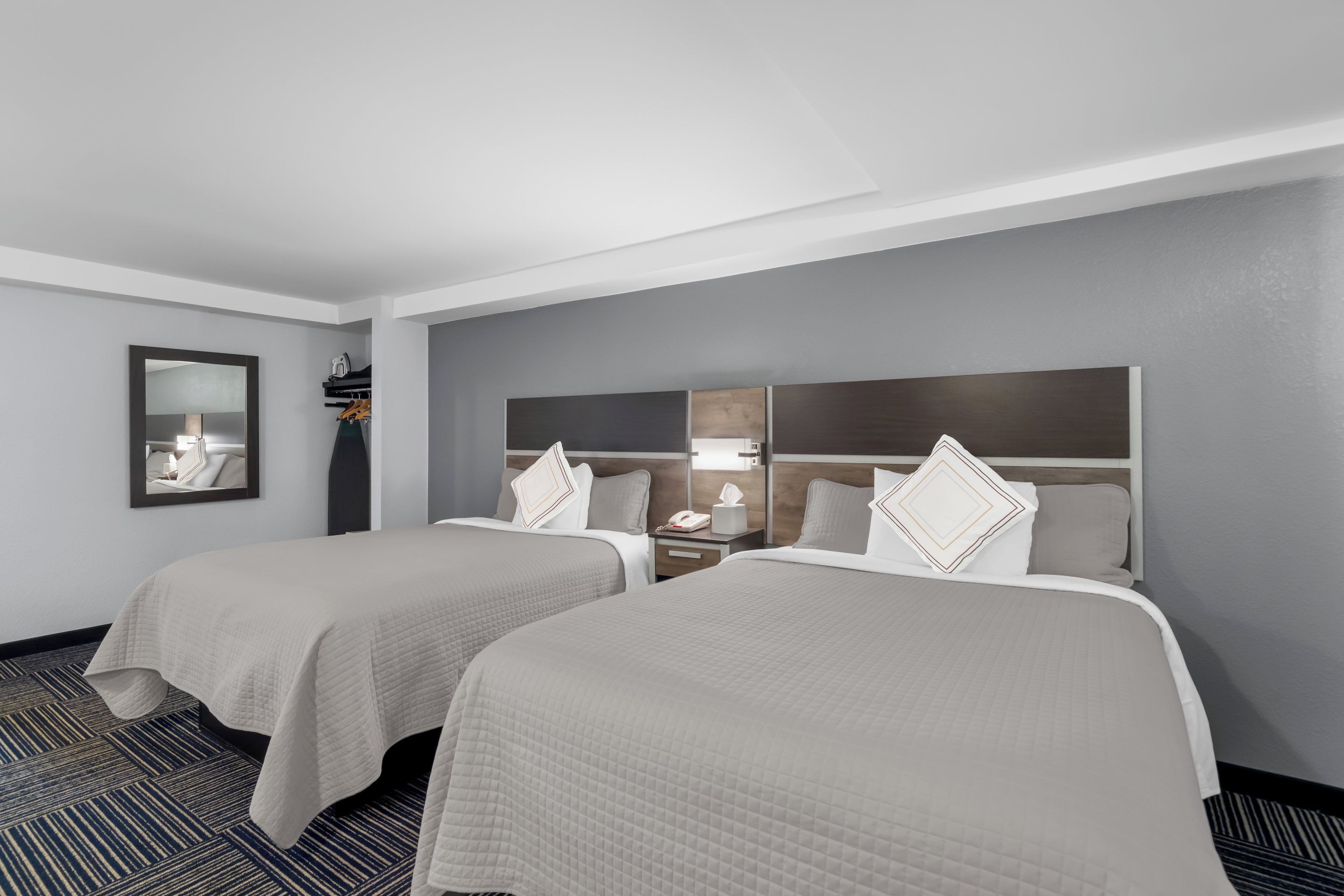 A hotel room with two beds, a nightstand, a mirror, and a wardrobe.