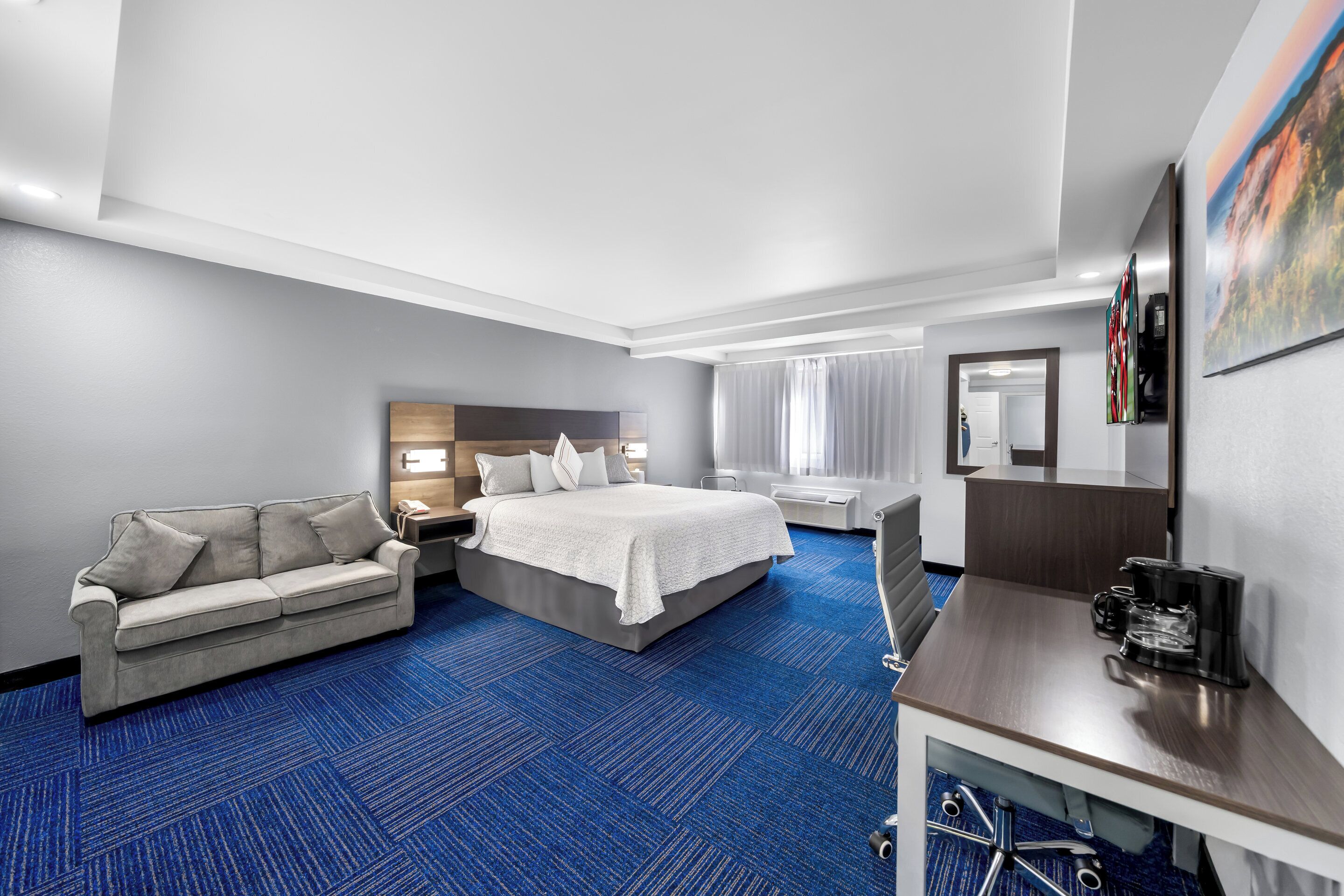 A hotel room with a bed, a sofa, a desk, and a coffee maker.