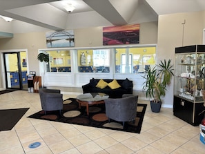 Un hall con un sofá negro, dos sillones, una mesa de centro, una planta en maceta y un aparador con objetos decorativos.