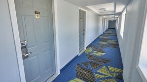 A hotel hallway with doors marked with room numbers, a patterned carpet, and a ceiling with recessed lighting. - Admiralty Inn & Suites - a Red Collection Hotel (East Falmouth)