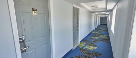 A hotel hallway with doors marked with room numbers, a patterned carpet, and a ceiling with recessed lighting.