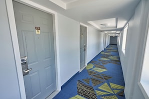 A hotel hallway with doors marked with room numbers, a patterned carpet, and a ceiling with recessed lighting. - Admiralty Inn & Suites - a Red Collection Hotel (East Falmouth)