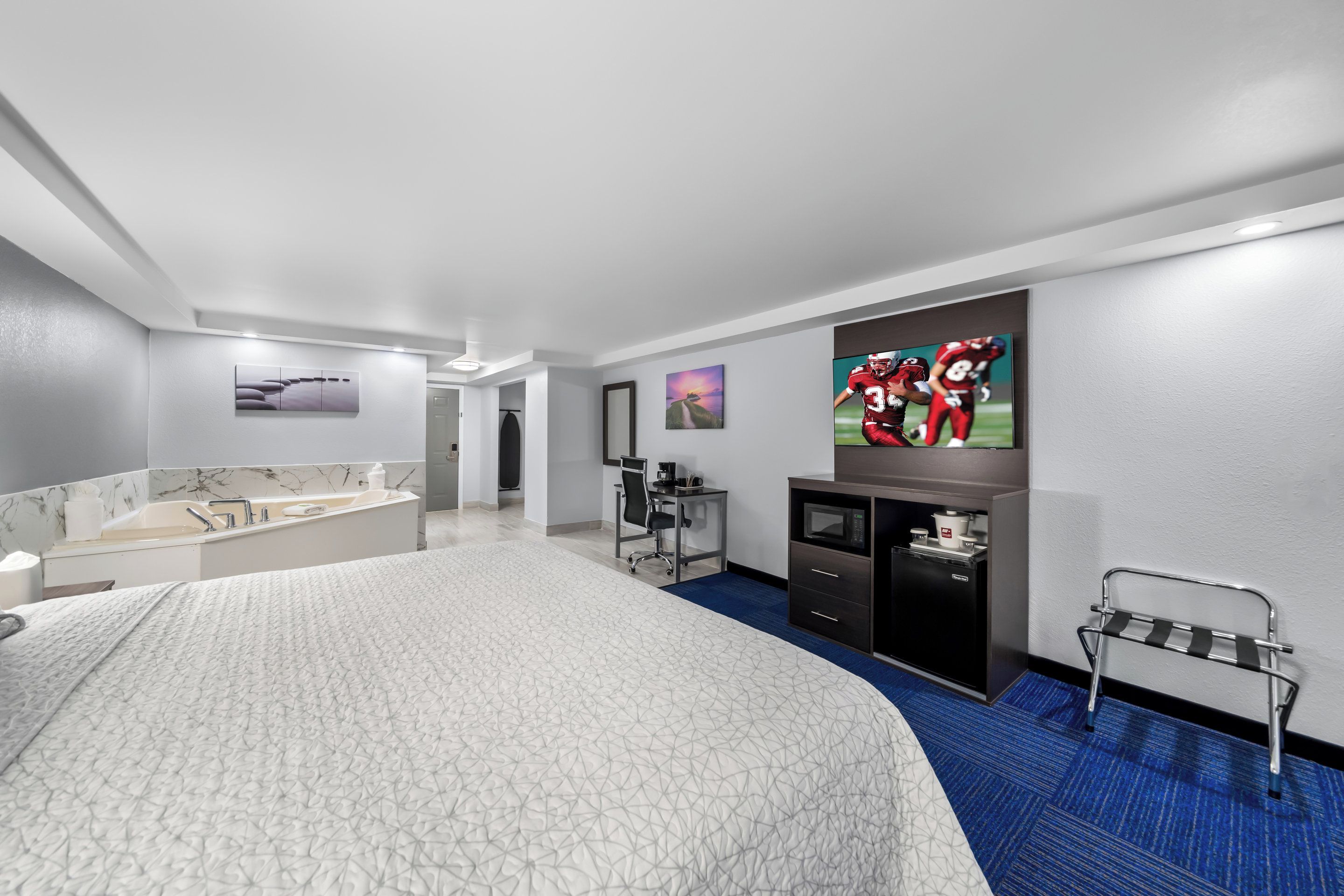 Habitación de hotel moderna con una cama grande, un baño con tocador de mármol, un escritorio con silla, un televisor en la pared y un banco junto a la ventana.